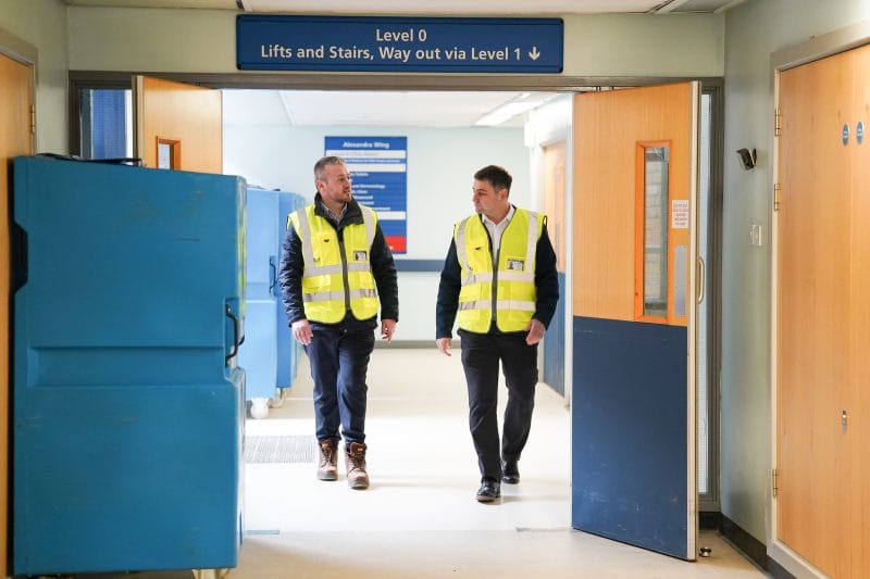 Two Axis CLC Group employees in high-visibility vests walking through a brightly lit corridor of a healthcare facility.