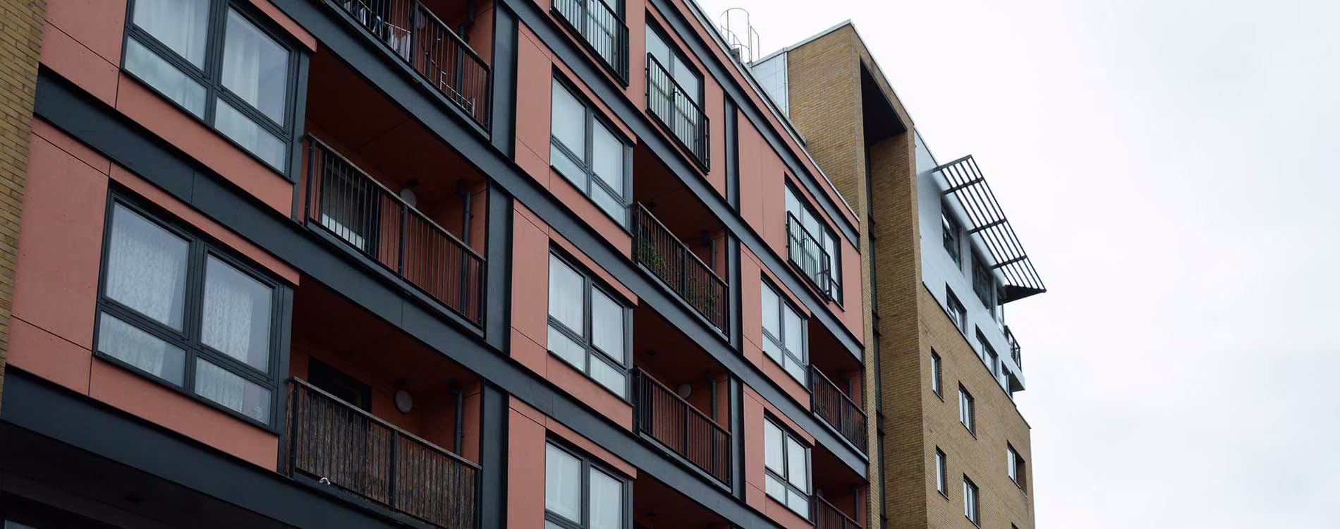 A low-angle view of a modern Peabody apartment block after a cladding replacement project, showing the new terracotta-coloured panels and black framework next to a yellow brick facade.