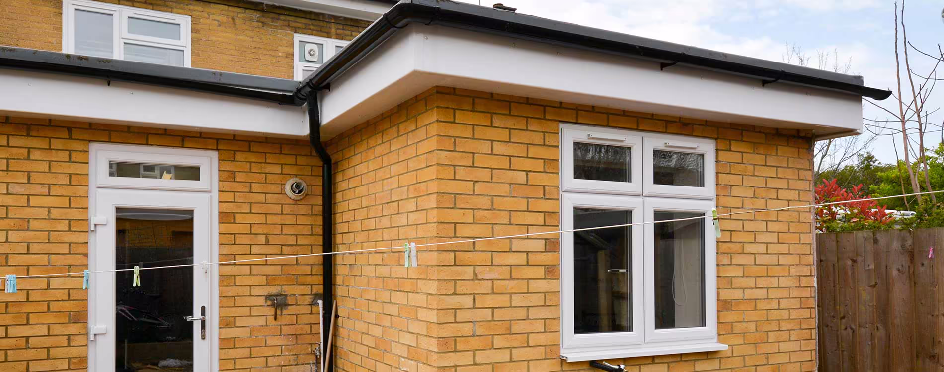 The exterior of a bespoke, single-storey house extension with light-coloured brickwork, a flat roof, and new white UPVC windows and doors.