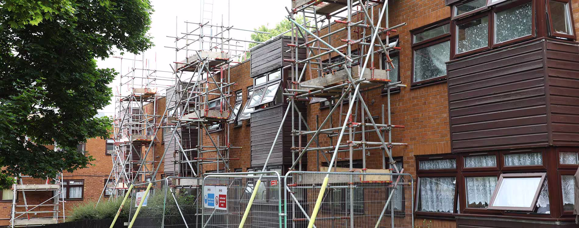 The exterior of a multi-storey residential block covered in extensive scaffolding during a major boiler installation and refurbishment project.