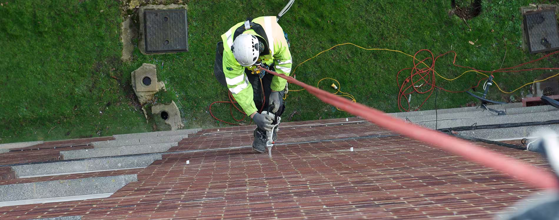 A top-down view of a specialist rope access technician abseiling down a tall building to drill holes for cavity wall insulation.