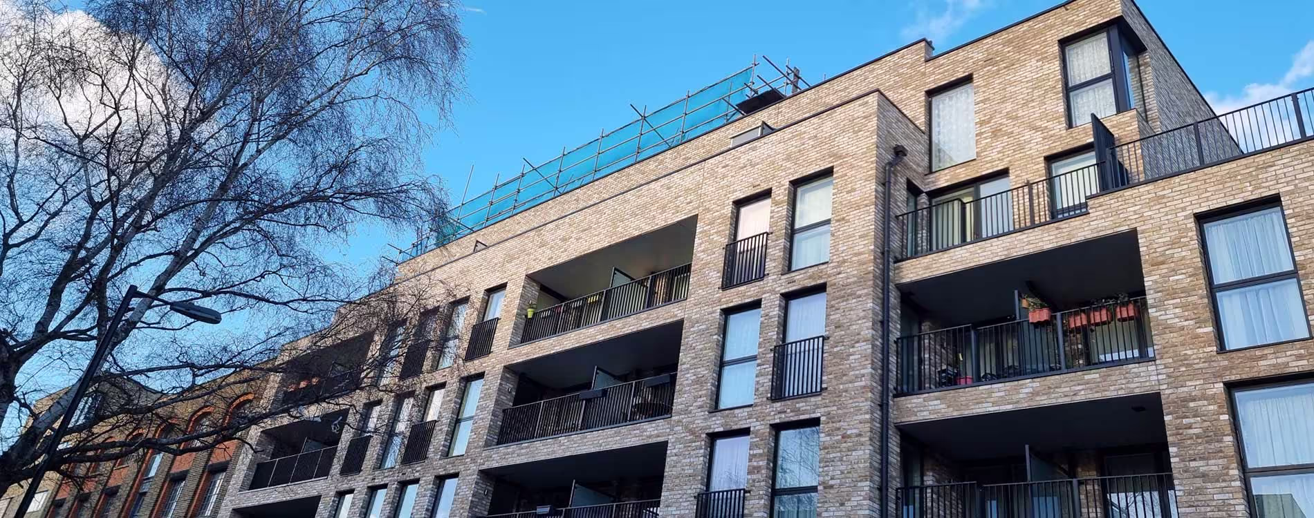 The exterior of a modern, multi-storey brick apartment building with balconies, showing the completed facade after a cladding replacement project.