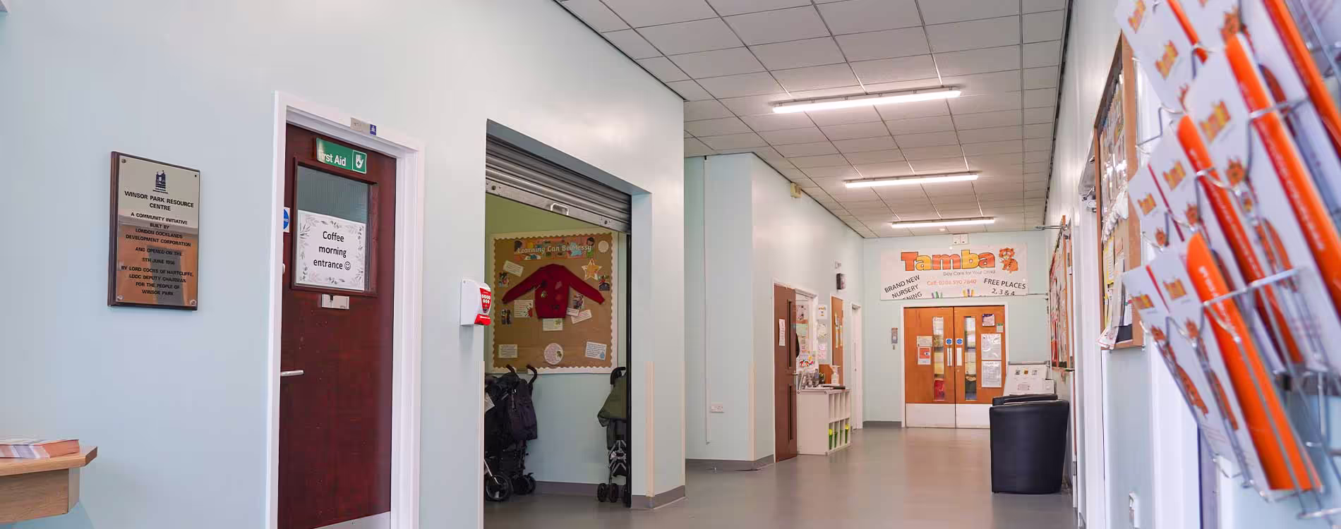 A long, brightly redecorated hallway in a community resource centre, showing newly painted walls, noticeboards, and entrances to various community services.