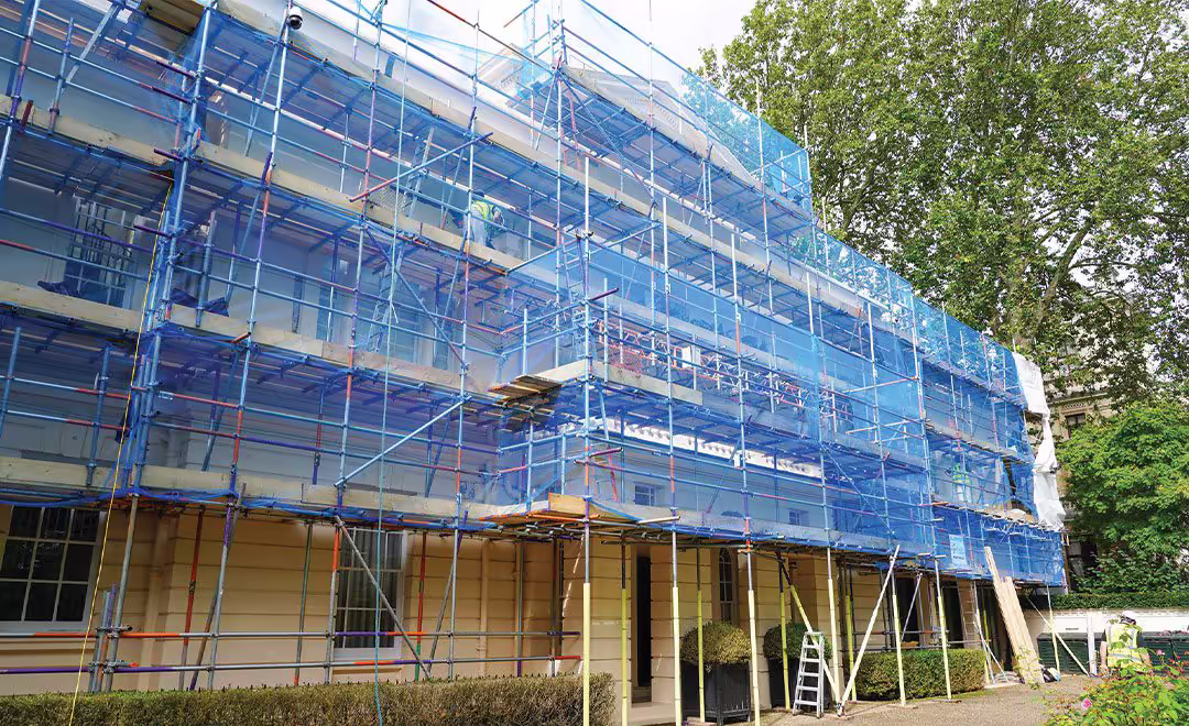 A large heritage building completely covered in scaffolding and blue safety netting during a major cyclical external decorations and restoration project.