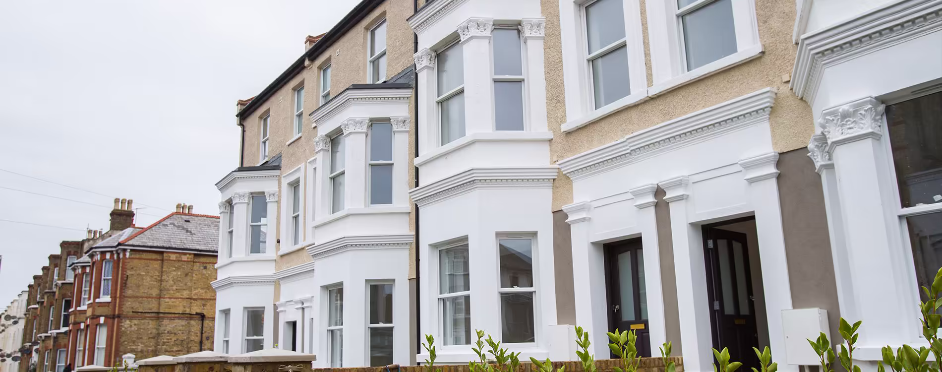 A row of beautifully restored Victorian terraced houses after a derelict property conversion project, showcasing the freshly painted white bay windows and architectural details.