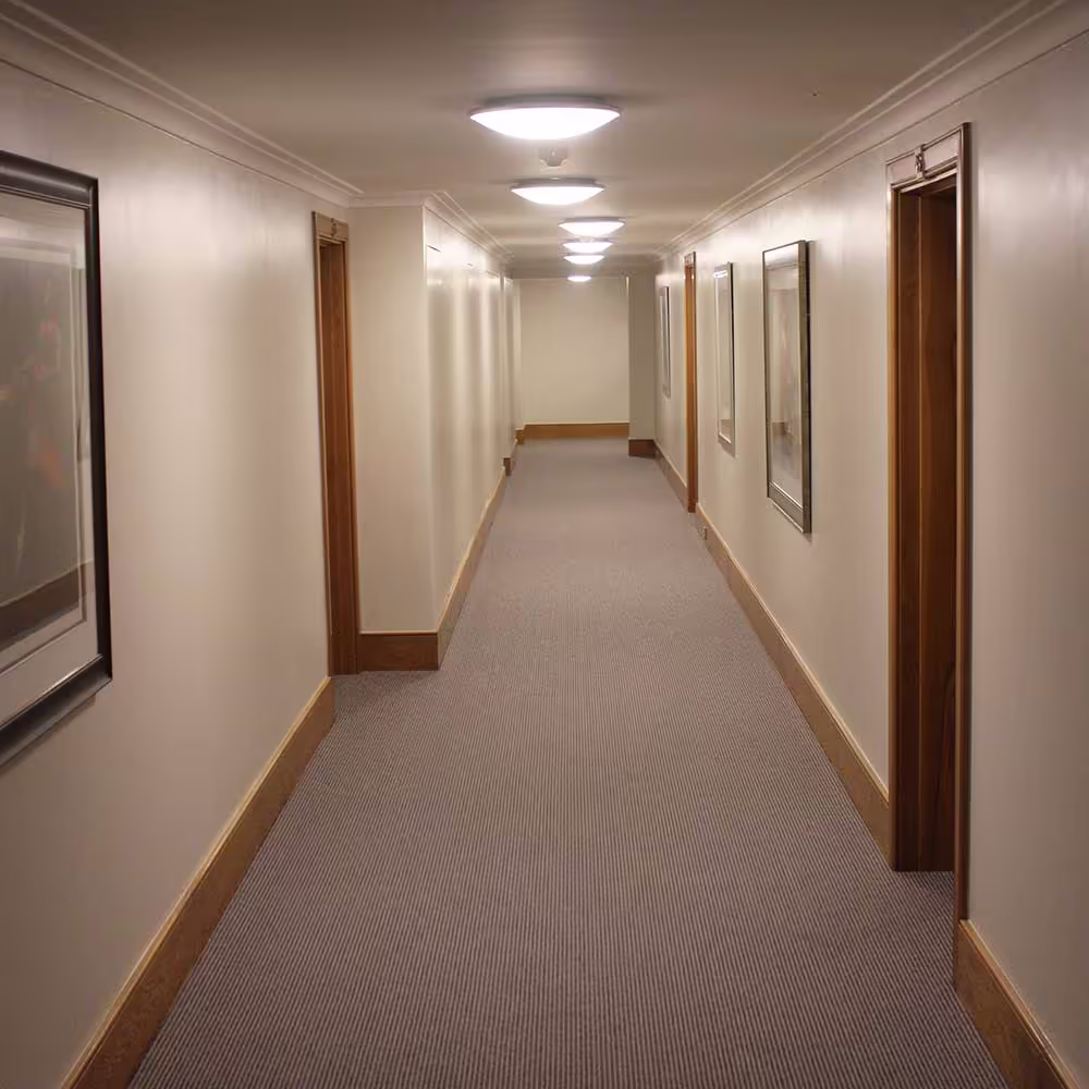 The interior of a long, impeccably restored corridor within a listed building, featuring plush grey carpeting, wood trim, and warm lighting.