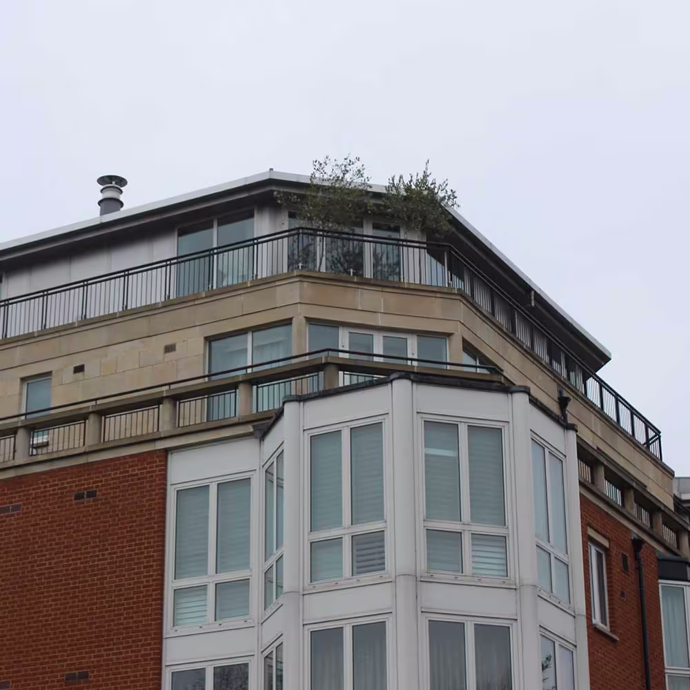 Close-up of the modern architectural extension to a listed building, showing a penthouse level with stone cladding and a rooftop terrace.