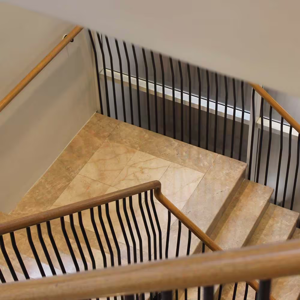 High-angle view of a restored marble staircase, highlighting the unique wavy black metal spindles and polished wooden handrail of the balustrade.