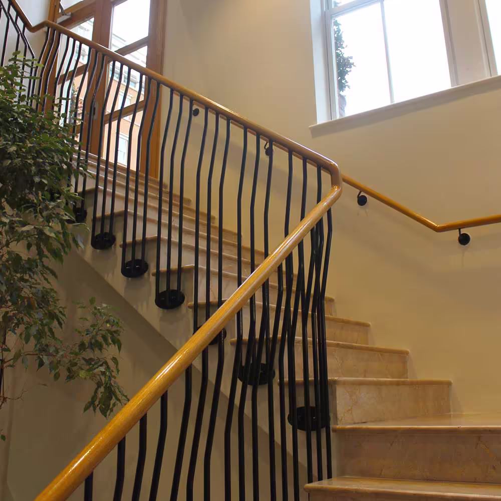 Elegant restored staircase in a Grade II listed building, featuring marble steps and a distinctive custom-made balustrade with wavy black metal spindles.