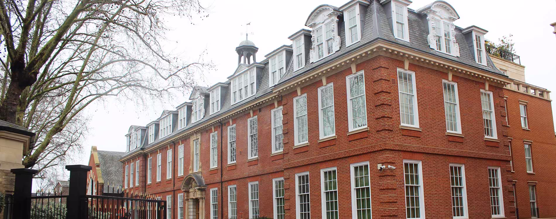 Panoramic view of a magnificently restored Grade II listed red brick building, showcasing its ornate dormer windows, cupola, and traditional sash windows.