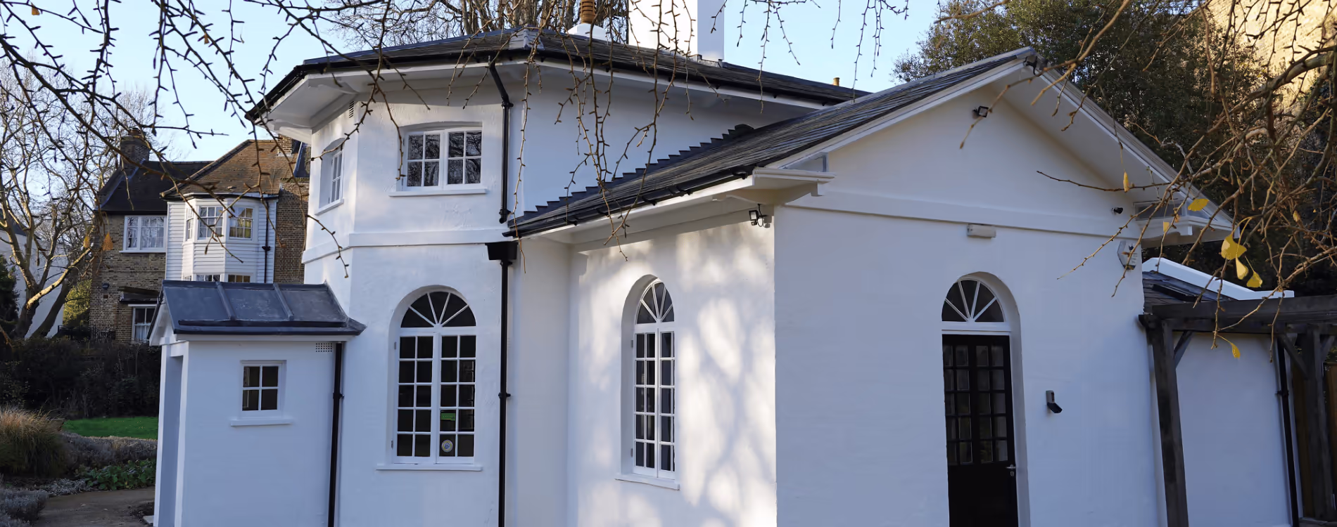 The beautifully refurbished exterior of a Grade II listed white building, showcasing the new slate roof, black guttering, and restored arched windows after a full renovation.