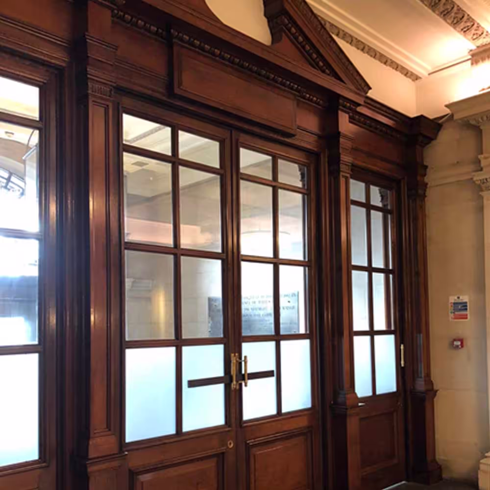A set of beautifully restored internal heritage doors in a Grade II listed building, featuring rich, dark wood frames and frosted glass panels.