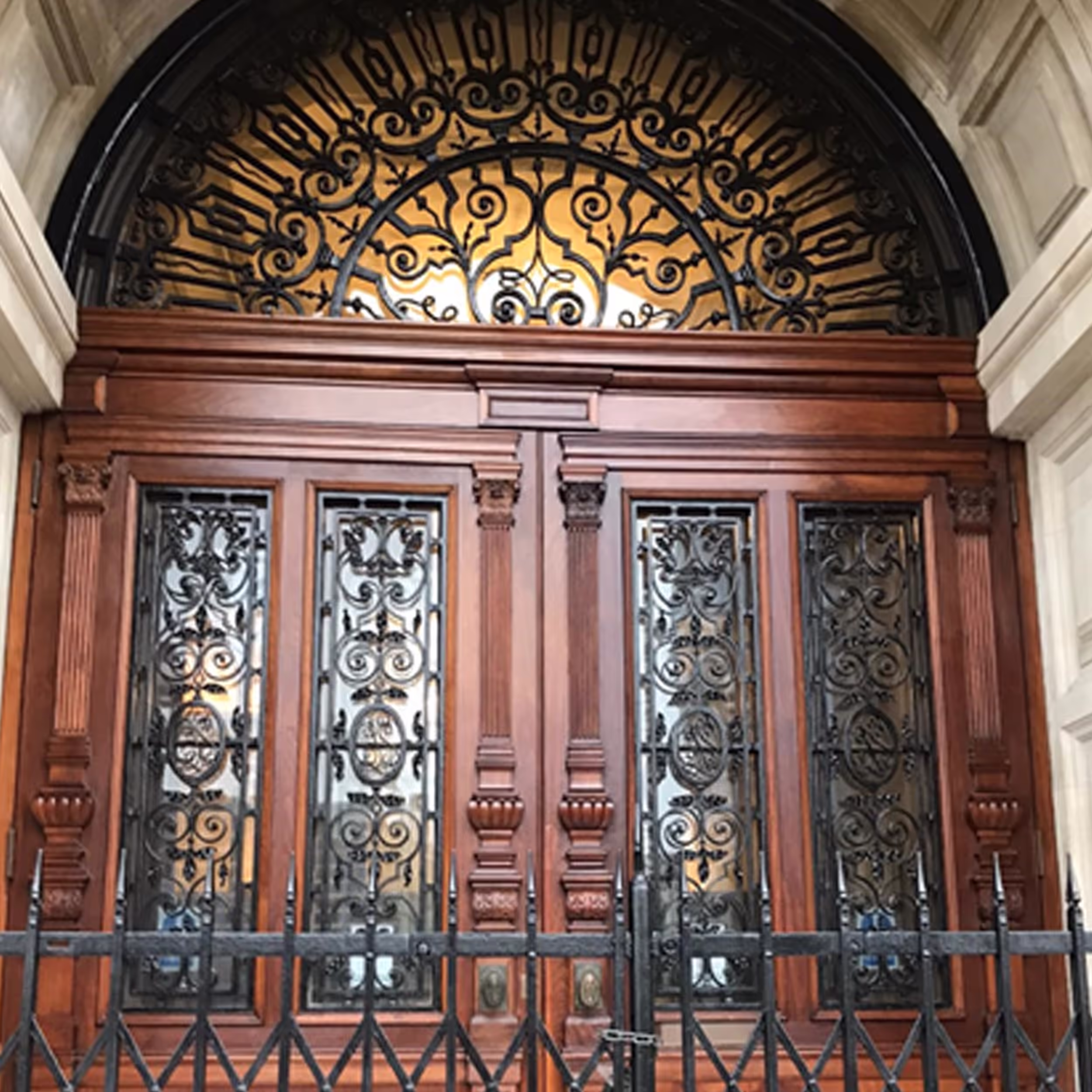 The grand entrance of a Grade II listed building, showcasing the meticulously restored double wooden doors with ornate iron grilles and an impressive fanlight.
