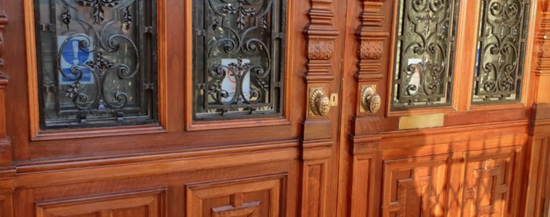 A close-up of a magnificently restored Grade II listed wooden entrance door, showing intricate carvings and decorative ironwork grilles after expert restoration.
