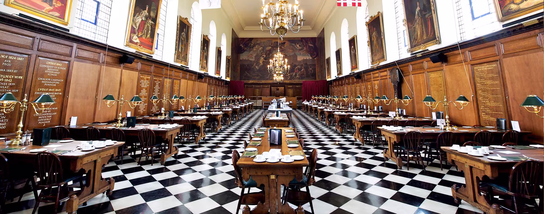 Panoramic view of a grand, refurbished heritage dining hall with a distinctive black and white chequerboard floor, wood-panelled walls, and long dining tables.