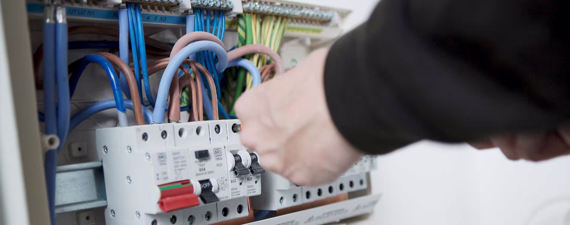 Close-up of a qualified electrician's hands performing safety checks and wiring on a domestic consumer unit for housing compliance services.