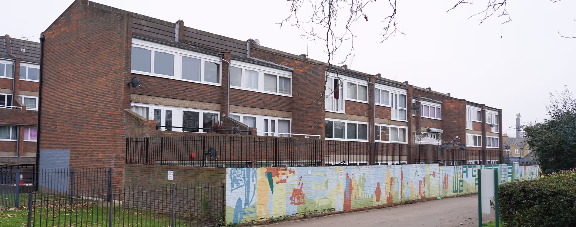 The exterior of a large brick housing estate which has undergone a planned external and communal decorations programme, with a colourful community mural on a boundary wall.