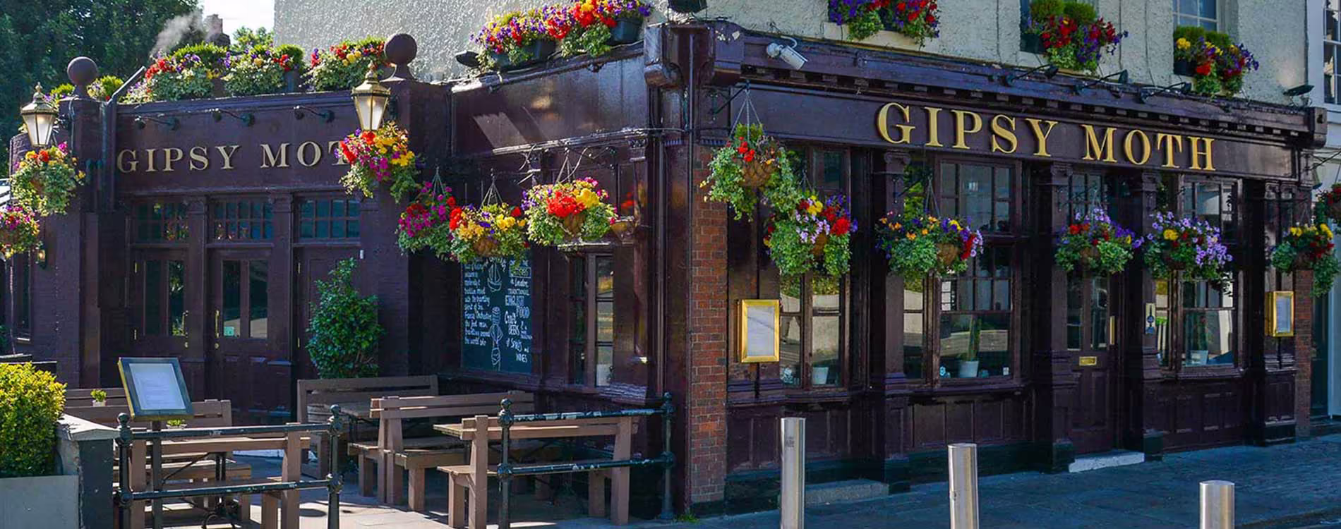 The beautifully refurbished exterior of the Gipsy Moth pub in Greenwich, featuring its traditional dark wood facade, gold lettering, and numerous colourful hanging flower baskets.