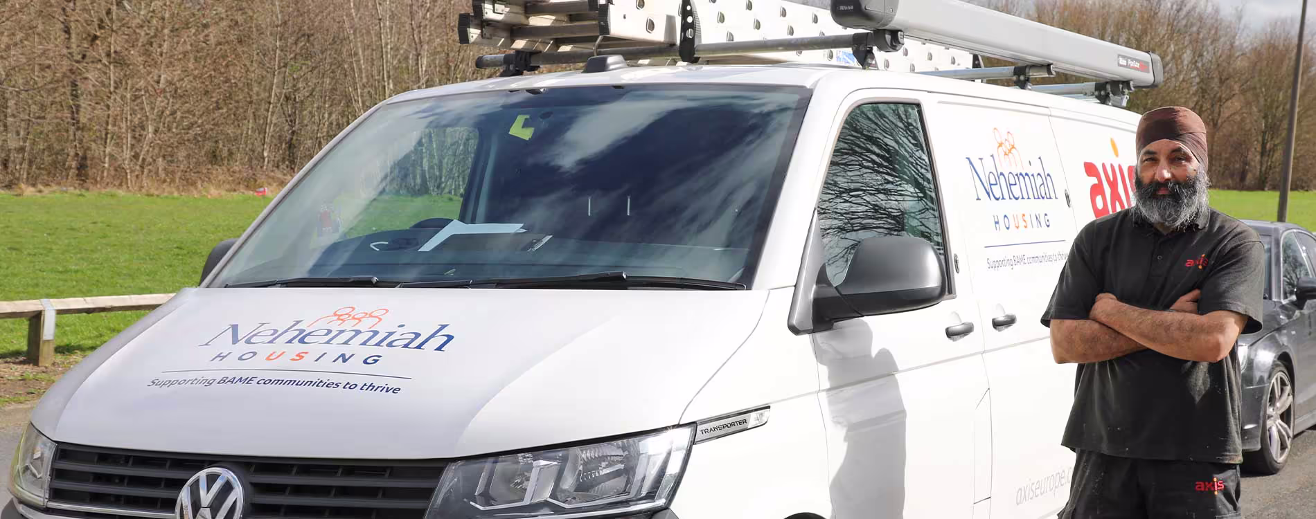 An Axis operative stands proudly with his arms crossed in front of a van co-branded with the Axis and Nehemiah Housing logos, representing their repair service contract partnership.