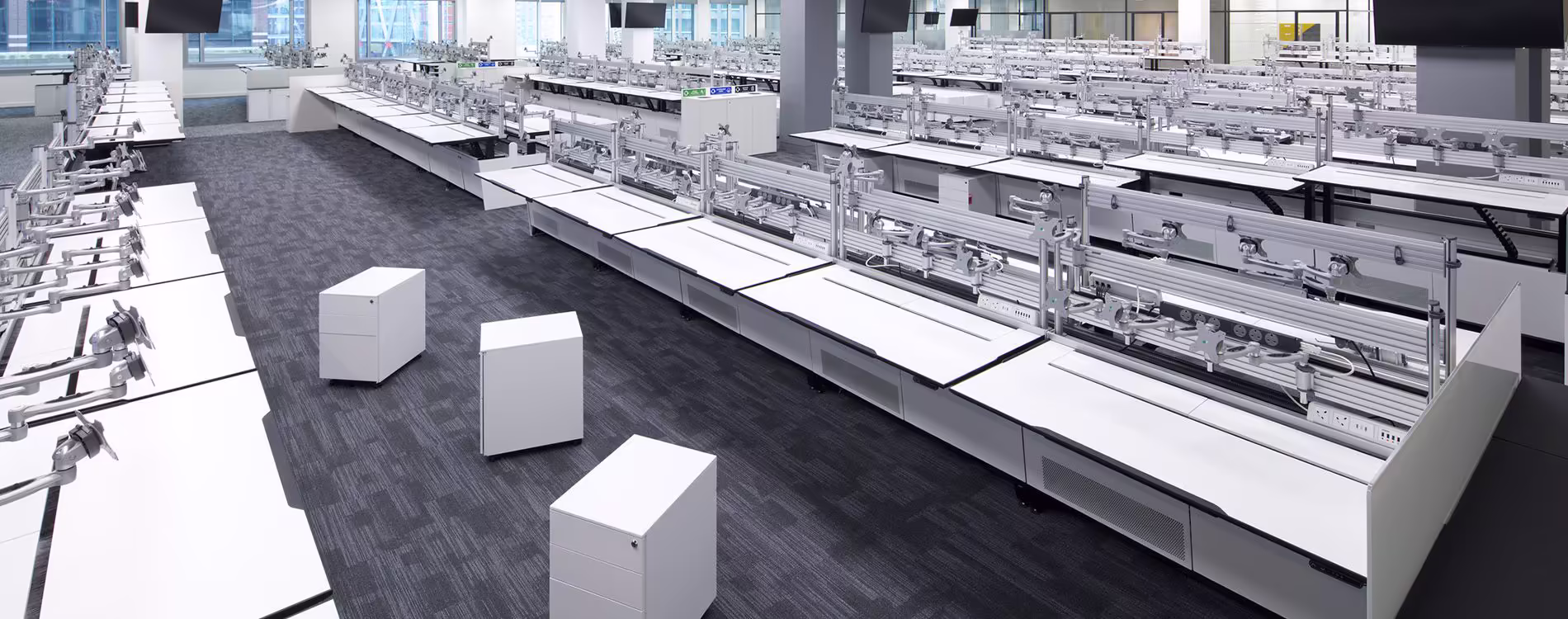 An aerial view of a large, modern trading floor or call centre office after major refurbishment, featuring long rows of white desks with monitor arms and minimal equipment, ready for the final technology fit-out following UPS removal and electrical works.