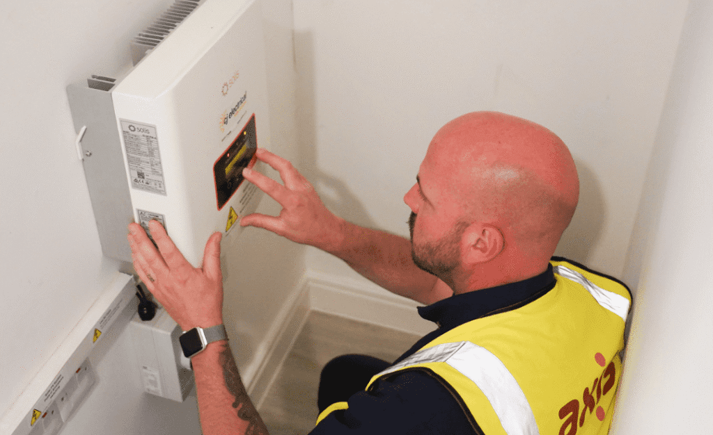 Workman with Axis vest, using his hands on an electrical system inside. Walls are white.