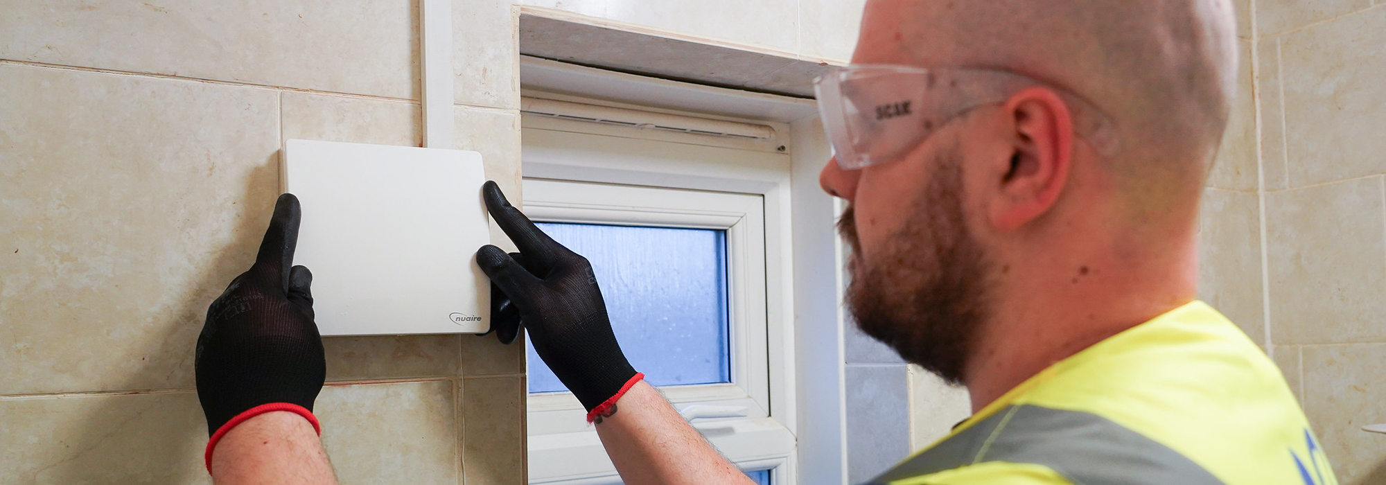 operative in high vis, safety glasses and gloves installing new ventilation into a residential bathroom