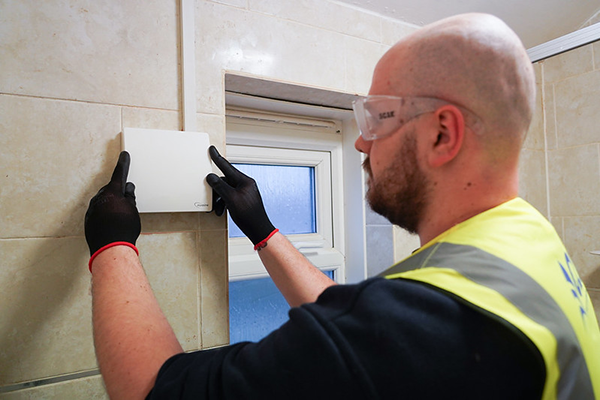 operative in high vis, safety glasses and gloves installing new ventilation into a residential bathroom