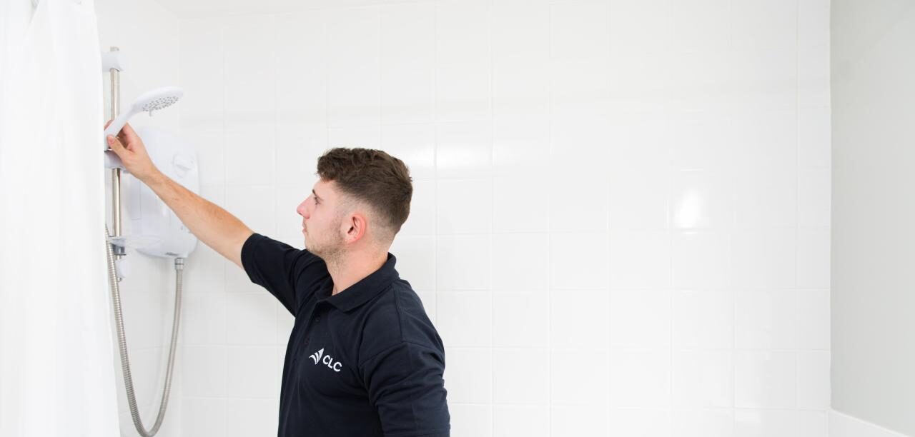 Operative in dark blue uniform installing a shower in a white tiled wet room