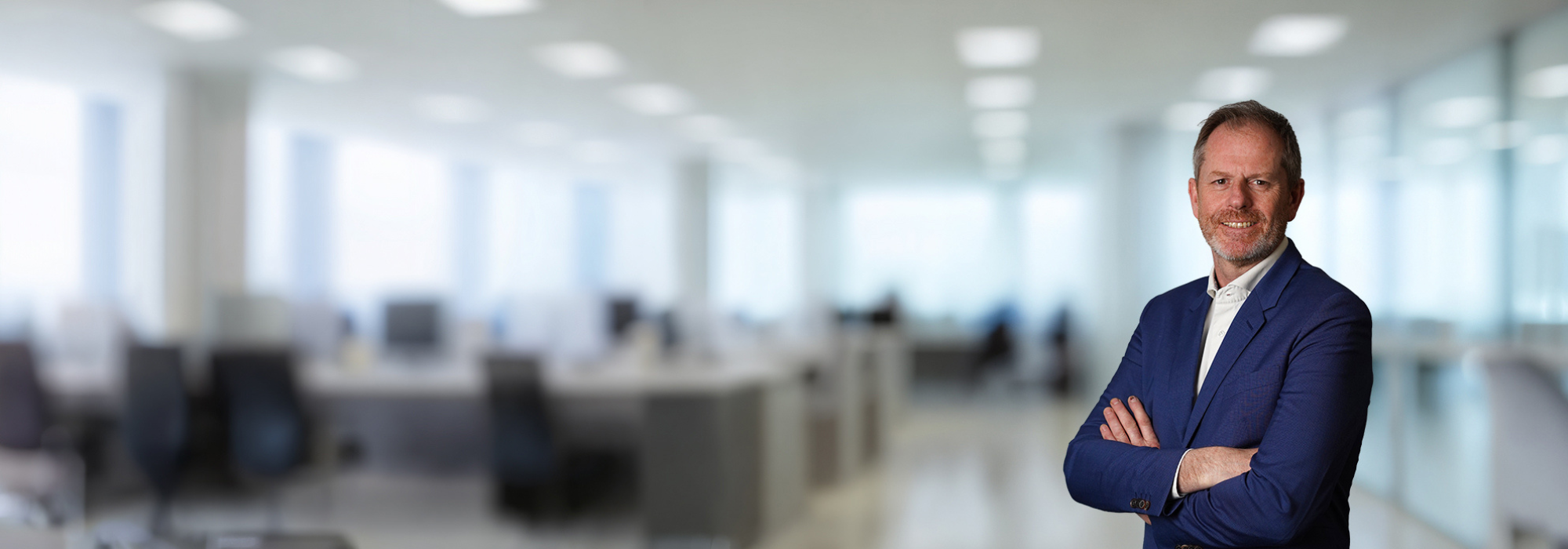 Smiling man in blue suit and a white shirt. With an office background behind. 