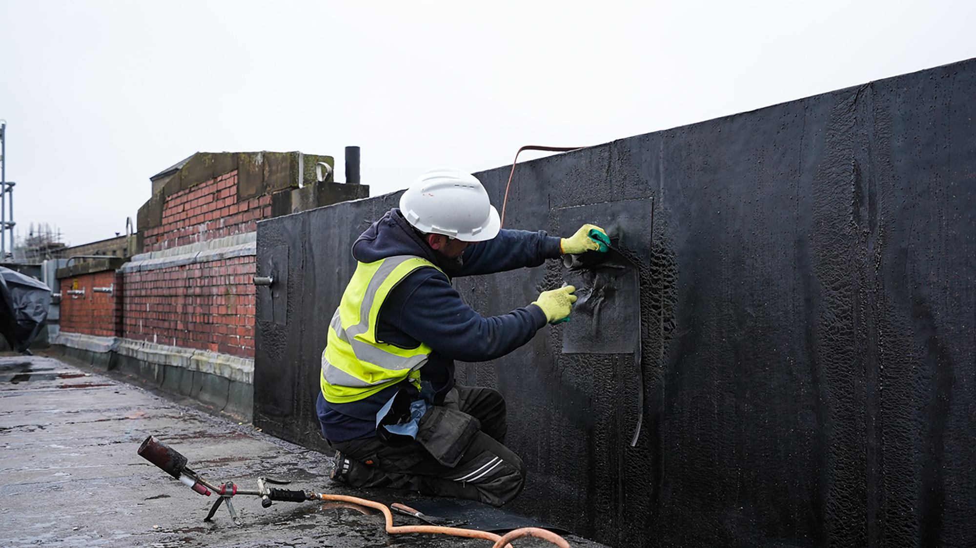 operative on hospital roof completing decarbonisation works in high vis, helmet and safety gloves