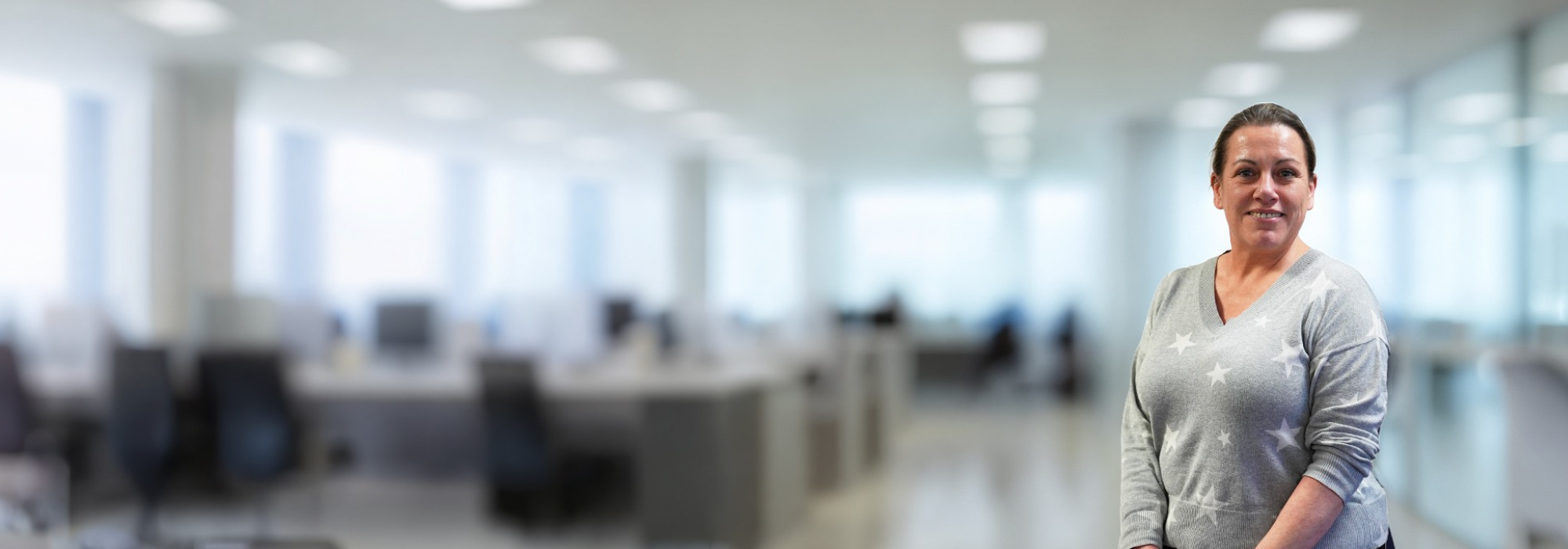 Smiling woman with a grey jumper and white stars. Office background with table and chairs in the background