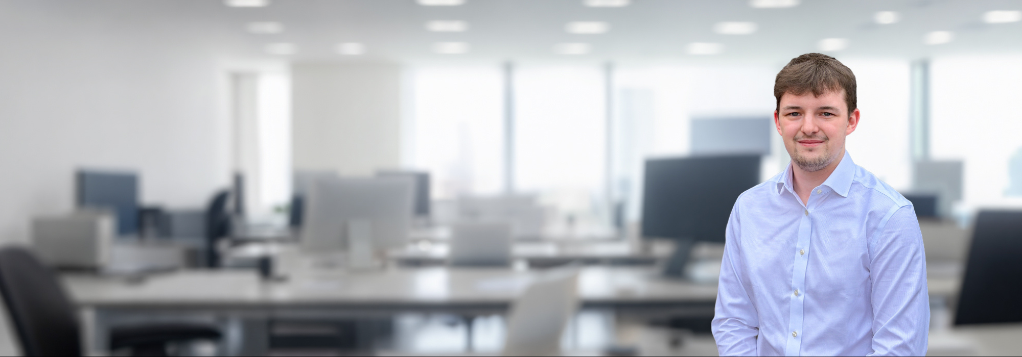 Apprentice boy in a shirt smiling. With an office of desk and chairs behind him 