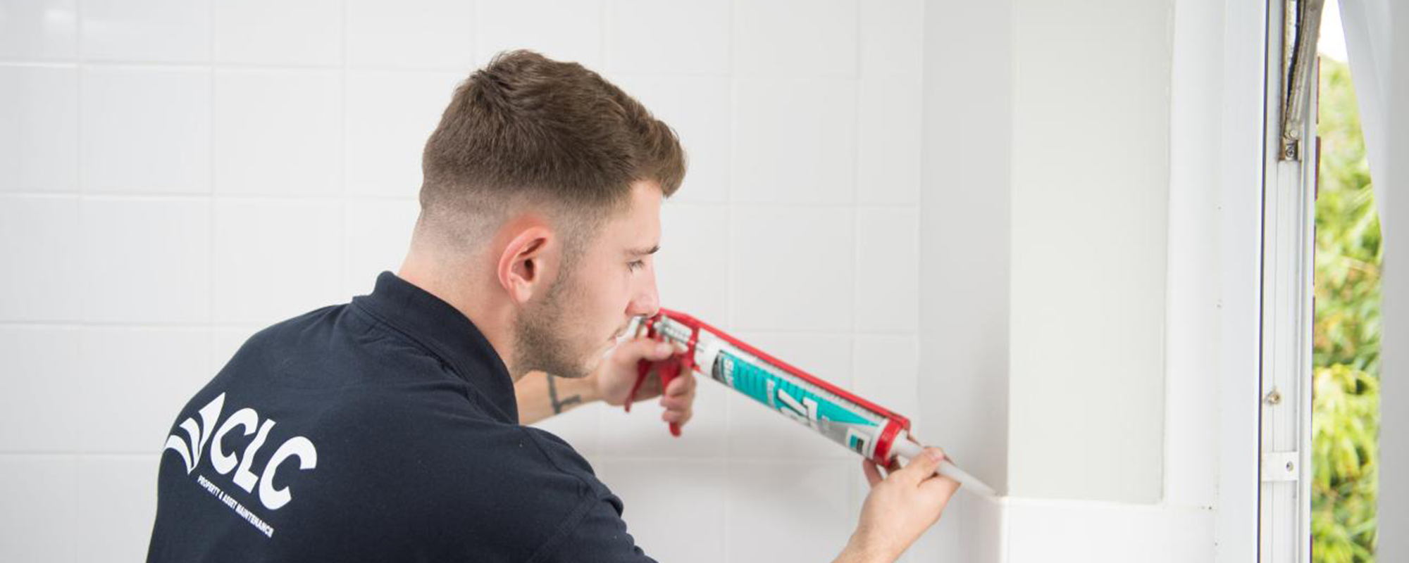operative in blue uniform applying seal to newly installed white tiled bathroom 
