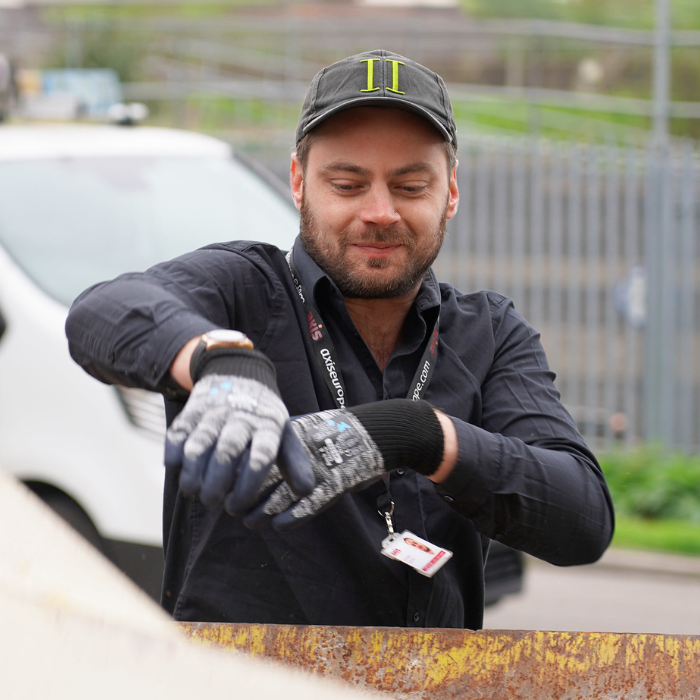 Man in black clothes, cap, and gloves throwing something in a skip