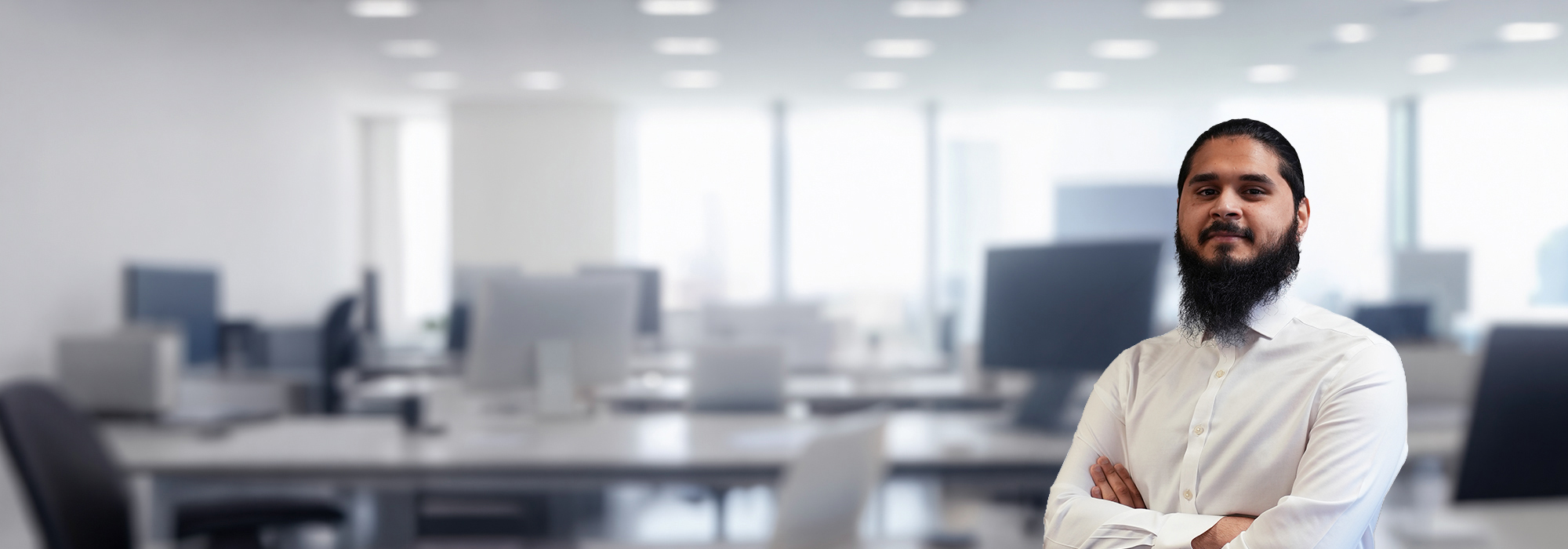 Man with black hair and beard, with a white shirt. Office background blur in the background