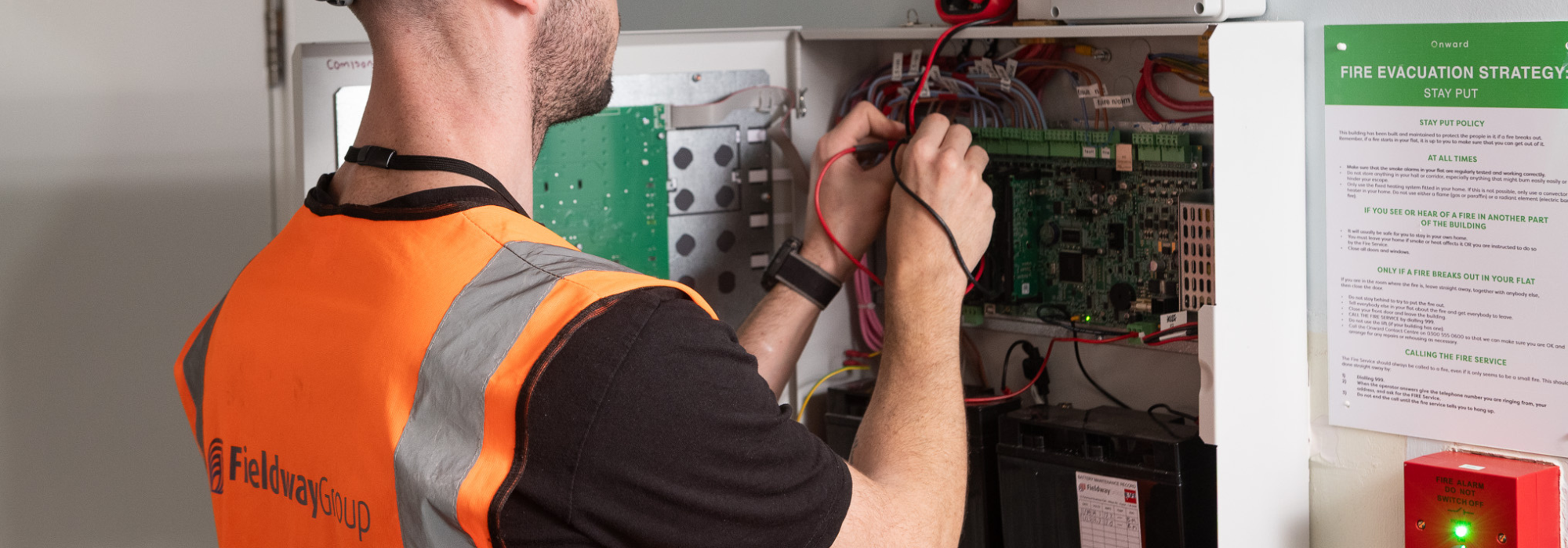 Man with orange vest, connecting wires. Logo of fieldway group