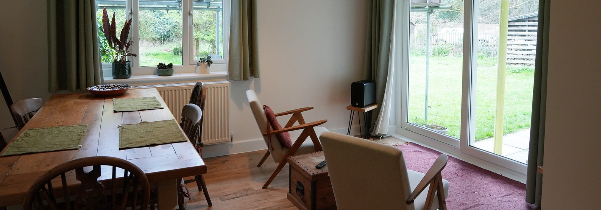 Inside a lodge with wooden table and chairs, carpet, two windows with green gardens