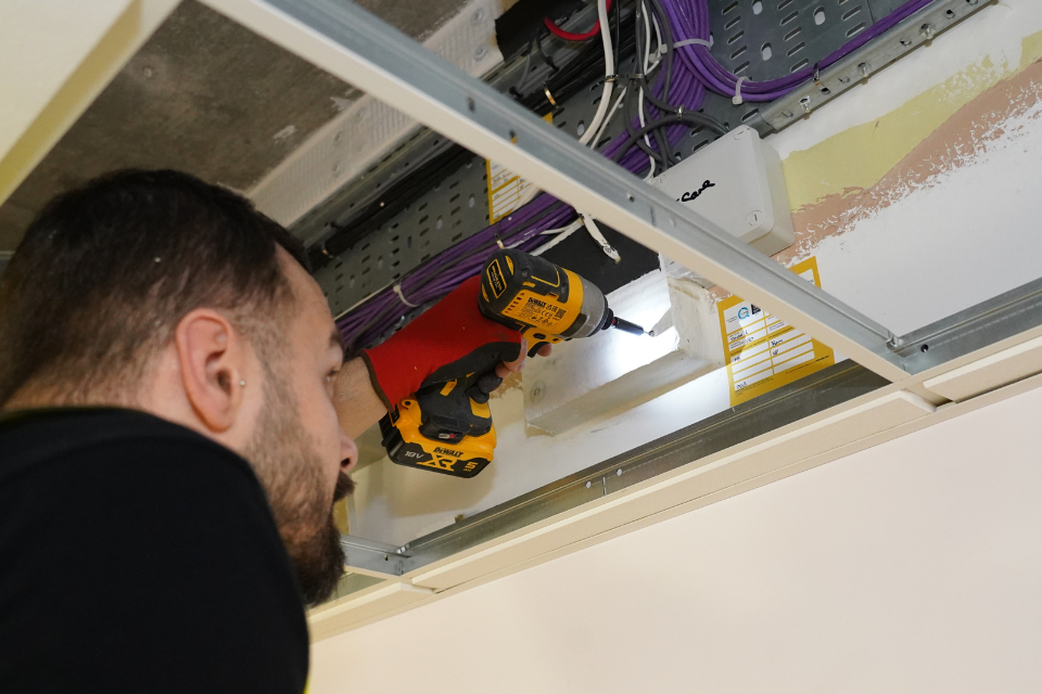 Man in high vis vest in roof cavity with silver pipes