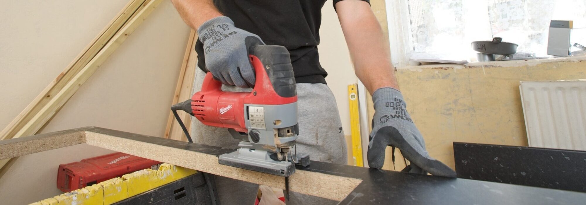 carpenter cutting into kitchen counter with jigsaw in residential void property